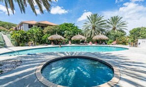 Relax by the pool surrounded by lush vegetation and lounge under a thatched umbrella.