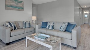 Una sala de estar con dos sofás grises, una mesa de centro y un cuadro de una playa.