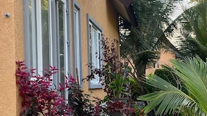 Una casa de fachada amarilla, con ventanas amplias y un jardín bien cuidado con diversas plantas y una escalera de piedra.
