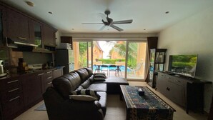 Una sala de estar con sofá, mesa de centro, televisor, espacio de cocina y vistas al exterior.