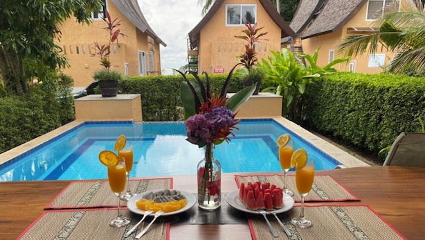 Una mesa de comedor con vista a la piscina, dos platos de comida y dos bebidas.