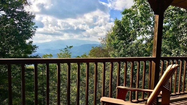 A wooden deck with a wooden chair and a railing overlooking a forested area with mountains in the distance. - O'Connors Retreat - Blowing Rock, Hot tub Secluded acreage, fabulous views (Lenoir)