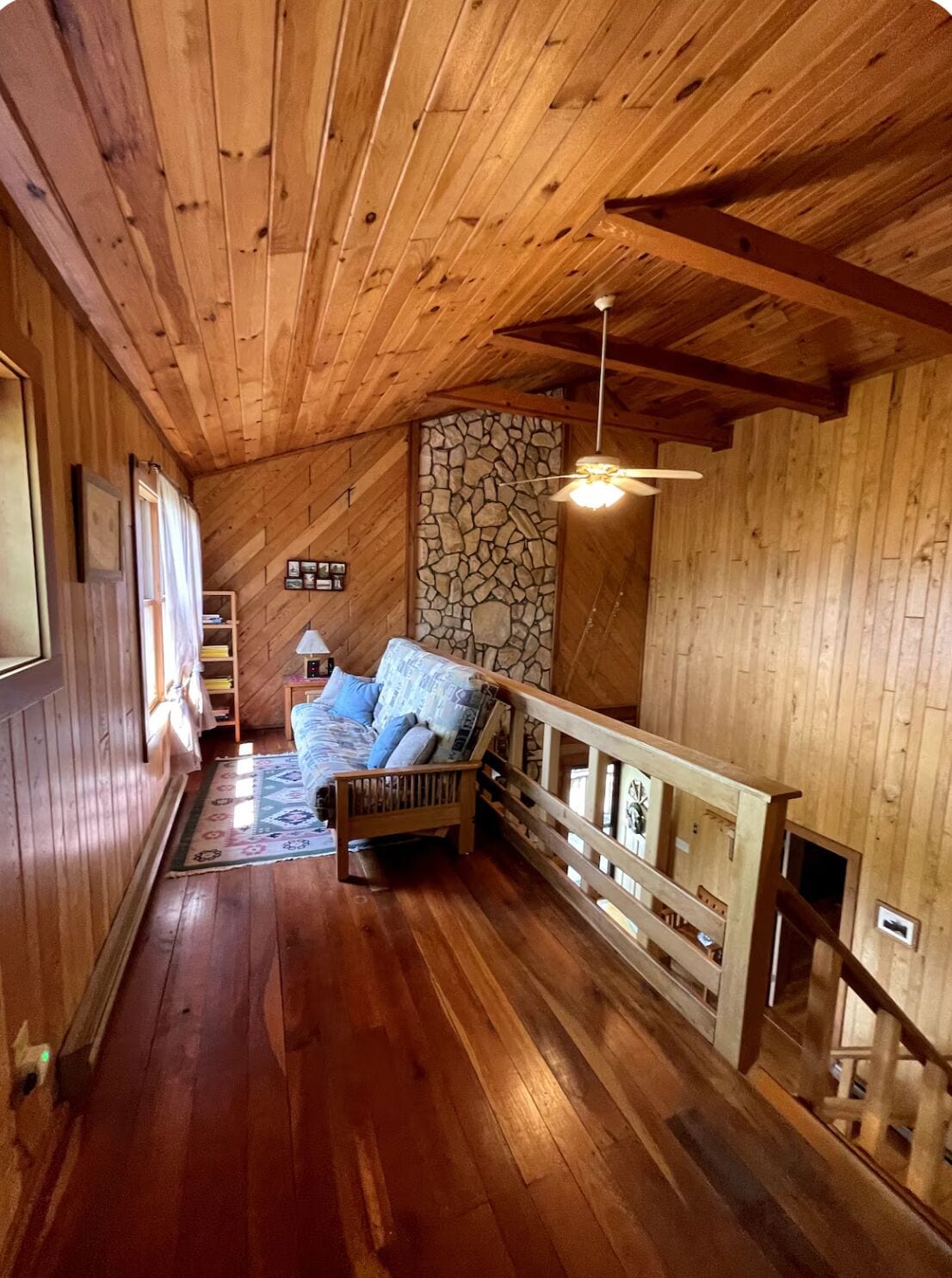 A wooden interior with a stone wall, a wooden bench, and a ceiling fan.