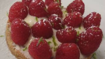 A white rectangular plate with a round pastry topped with raspberries and a white cream, garnished with green herbs.