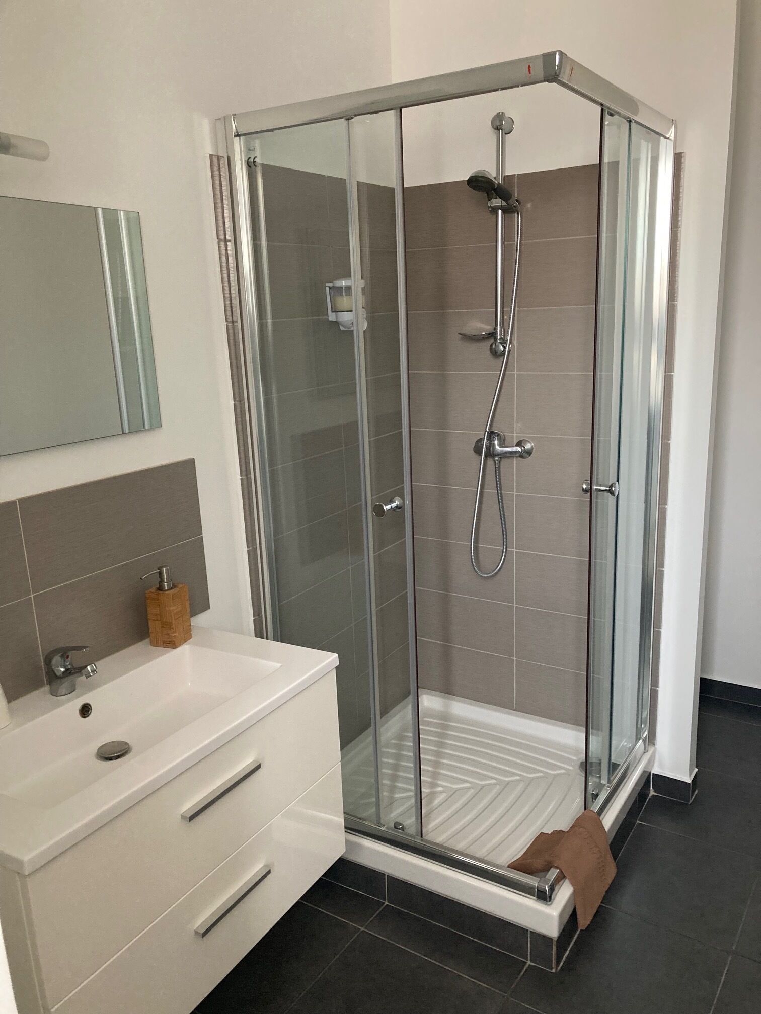 Une salle de bain moderne avec une douche à parois de verre, un meuble-lavabo blanc avec un miroir et un porte-serviettes.