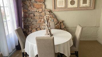 A dining area with a stone wall, a round table with a white tablecloth, and three chairs.