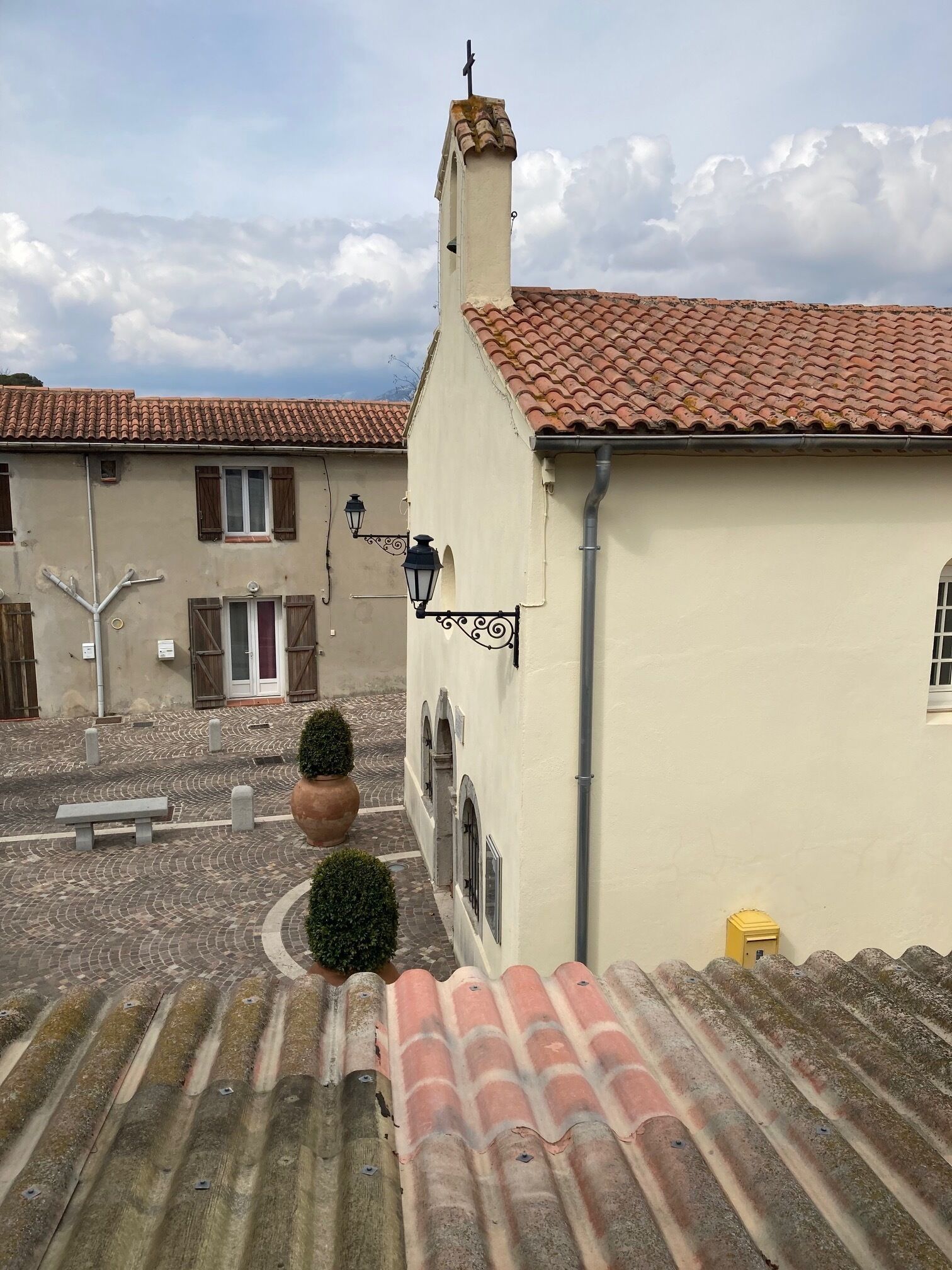 Une cour intérieure avec un bâtiment doté d’un toit recouvert de tuiles, d’une cheminée et d’un petit panneau.