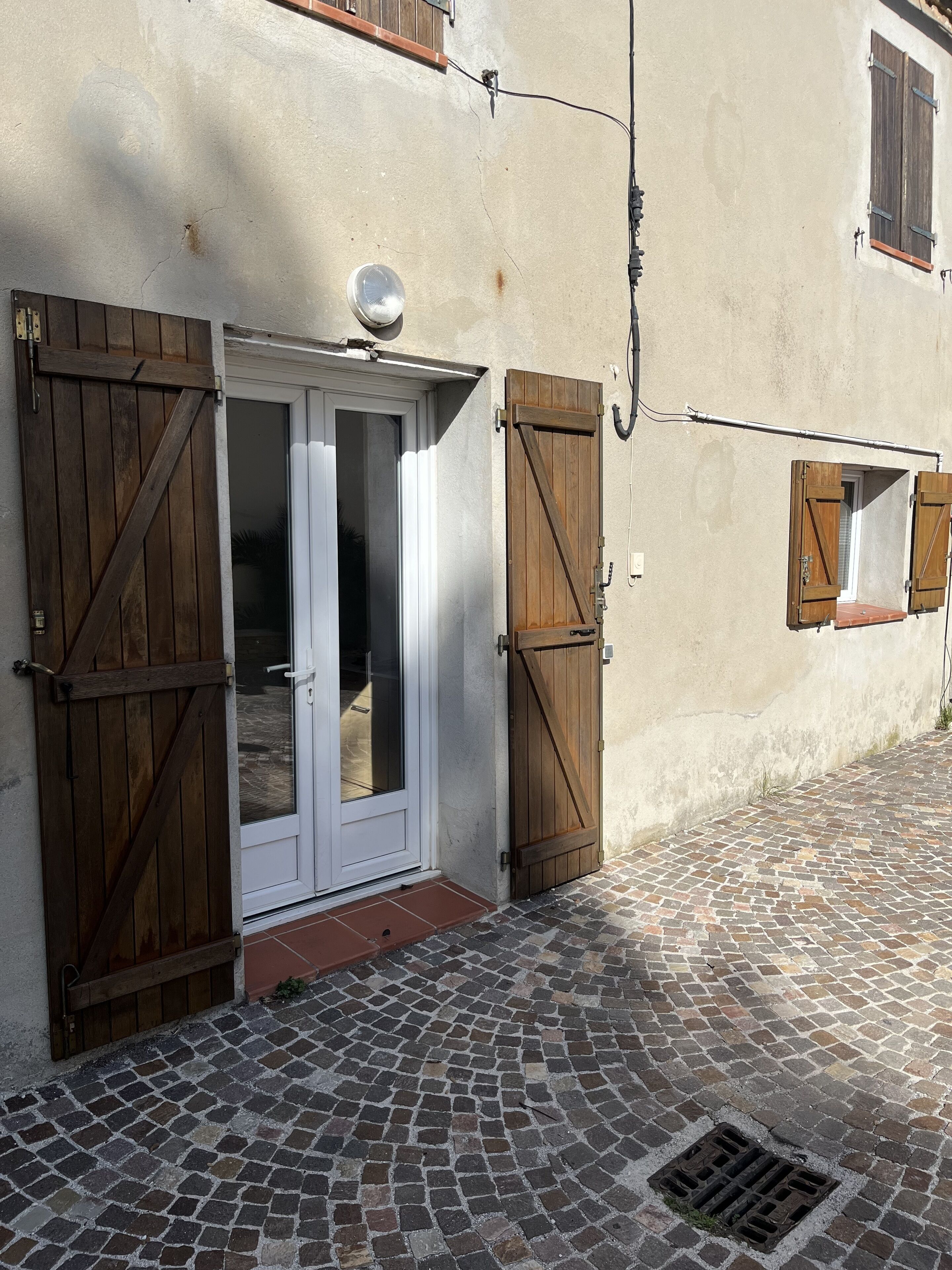 A building with a cobblestone entrance, wooden shutters, and a metal door.