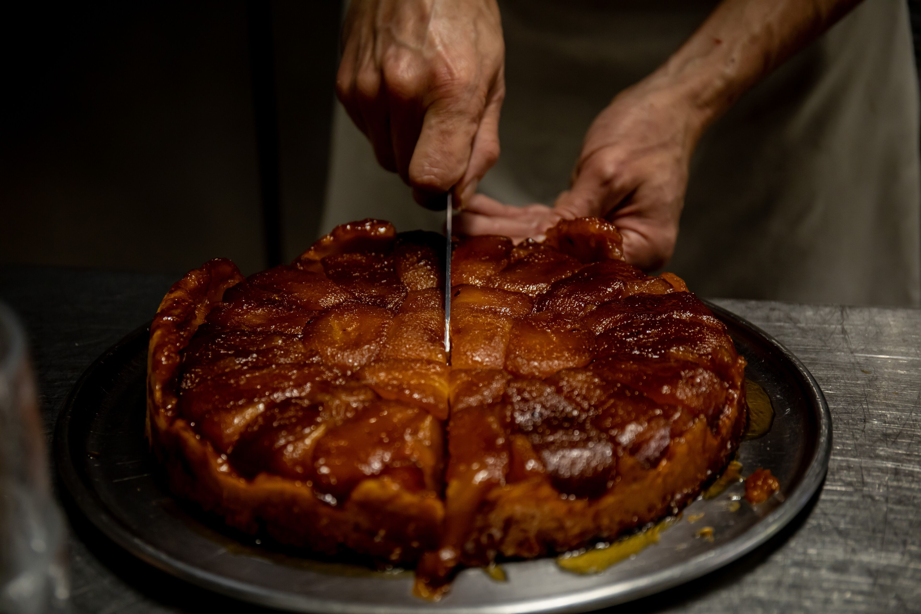Una persona cortando un pastel glaseado sobre un plato de metal.