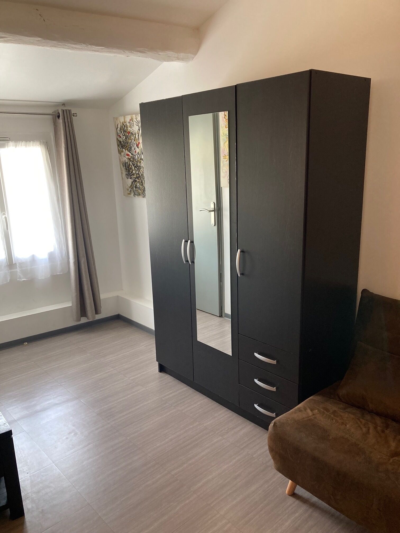 Una habitación con un armario grande, un sofá marrón y una ventana con cortinas.