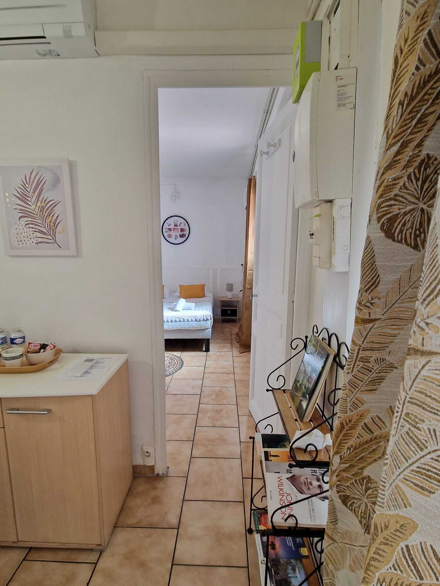 A narrow hallway leading to a bedroom with a bed and a nightstand. A small table with a tray of items is visible on the left.