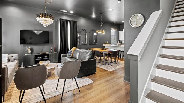 Una sala de estar moderna con sofá, una mesa de comedor y sillas, una zona de cocina y una escalera.