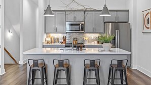 Una cocina moderna con armarios grises, electrodomésticos de acero inoxidable y una isla central con taburetes de bar.