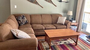 A living room with a brown sofa, two decorative paddles on the wall, a wooden coffee table, and a colorful rug. - Spacious Year Round Condo Retreat to the White Mountains (North Conway)