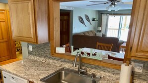 A kitchen with granite countertops, a stainless steel sink, wooden cabinets, and a large mirror reflecting a dining area with a couch and chairs. - Spacious Year Round Condo Retreat to the White Mountains (North Conway)