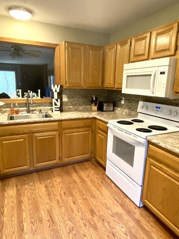 Una cocina con armarios de madera, una estufa blanca, un microondas y una encimera de granito.