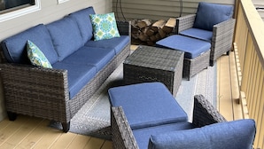 A covered patio with wicker furniture, including a sofa and ottomans, and a fire pit. - Spacious Year Round Condo Retreat to the White Mountains (North Conway)