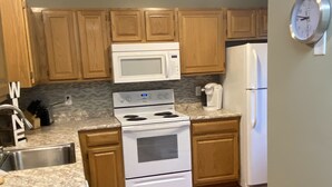 A kitchen with wooden cabinets, a white stove, a microwave, a refrigerator, and a clock on the wall. - Spacious Year Round Condo Retreat to the White Mountains (North Conway)