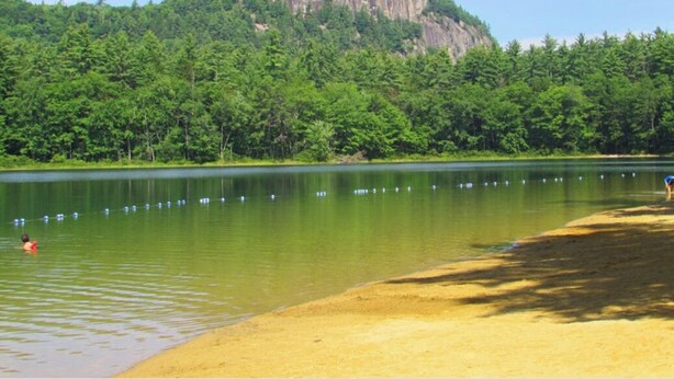 A lake with a sandy beach and a forested hill in the background. - Spacious Year Round Condo Retreat to the White Mountains (North Conway)