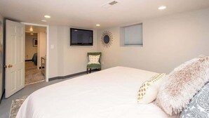 A bedroom with a large bed, a television mounted on the wall, a chair, and a door leading to another room. - Downtown Fargo Gem: Full Home for Large Groups (Fargo)
