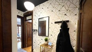 A hallway with a geometric-patterned wall, a coat rack with a jacket, a small table with a plant, and a framed picture. - Historic Condo in Downtown Fargo (Fargo)