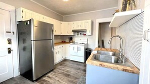 A compact kitchen with white cabinets, a stainless steel refrigerator, a gas stove, and a sink with a wooden countertop. - Historic Condo in Downtown Fargo (Fargo)