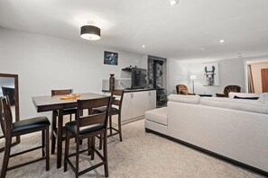 A modern living room with a sofa, a dining table with chairs, a kitchen area with a stove, and a TV.