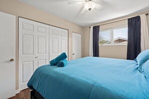 A bedroom with a bed, a ceiling fan, a window with curtains, and a door.