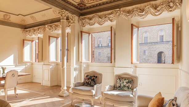 Een ruime woonkamer met een hoge plafond, grote ramen en klassiek meubilair.