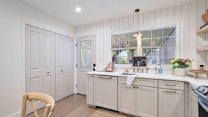 A kitchen with white cabinetry, a wooden chair, a woven rug, and a welcome sign. - Closest Stay to Downtown Mt Dora - Renovated - Walk Everywhere (Mount Dora)