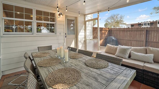 A covered patio with a wooden table set for dining, surrounded by wicker chairs and a cushioned bench. - Closest Stay to Downtown Mt Dora - Renovated - Walk Everywhere (Mount Dora)
