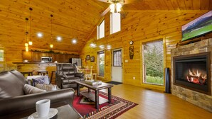 A spacious living room with a fireplace, leather sofa, and a television mounted on the wall. - 7 min to Dollywood - Hot Tub - Arcades - Sunshine! (Pigeon Forge)