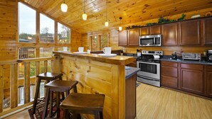 A wooden cabin kitchen with a bar area, large windows, and a view of the outdoors. - 7 min to Dollywood - Hot Tub - Arcades - Sunshine! (Pigeon Forge)