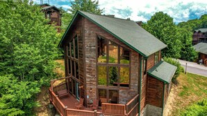 A wooden cabin with a balcony, surrounded by dense forest. - 7 min to Dollywood - Hot Tub - Arcades - Sunshine! (Pigeon Forge)