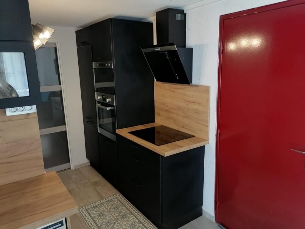A compact kitchen with black cabinetry, a wooden countertop, and a red door.
