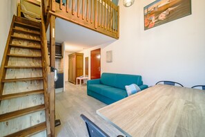 A spacious living area with a wooden staircase, a teal sofa, and a wooden dining table.