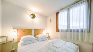 Ein Hotelzimmer mit zwei Betten, einem Holzkopfteil, einem Nachttisch mit Lampe und einem Fenster mit durchsichtigen Vorhängen.