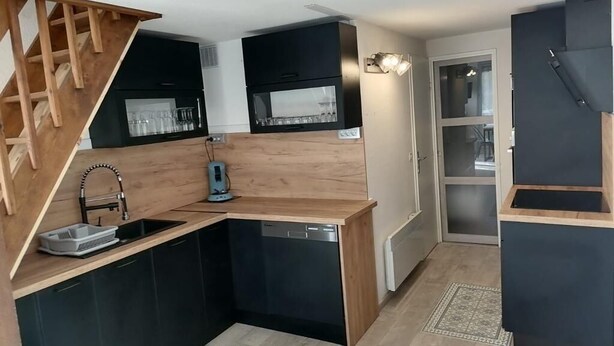 Eine kleine Küche mit einer Holztreppe, schwarzen Schränken und einem eingebauten Geschirrspüler.