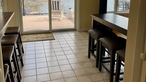A kitchen with a view of a lake, a sliding glass door, and a dining area with stools. - Lake Winnipesaukee Waterfront Beach & Dock (Moultonborough)