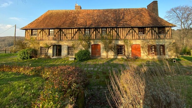 Une maison traditionnelle à colombages, avec des fondations en pierre, de nombreuses fenêtres et une grande porte d’entrée.