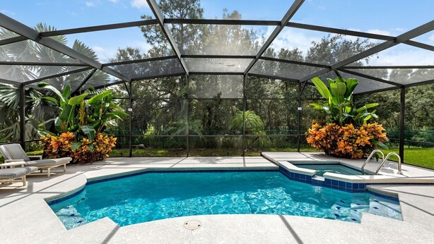 A covered outdoor swimming pool with lounge chairs and tropical plants. - Murano Mews (Kissimmee)