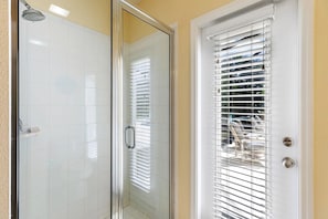 Bathroom features a glass shower enclosure and a door with horizontal blinds, a handheld showerhead, and a silver handle.