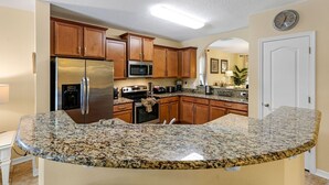 A kitchen with granite countertops, stainless steel appliances, wooden cabinets, and a microwave. - Murano Mews (Kissimmee)