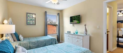 A bedroom with two beds, a ceiling fan, a TV, and a dresser.