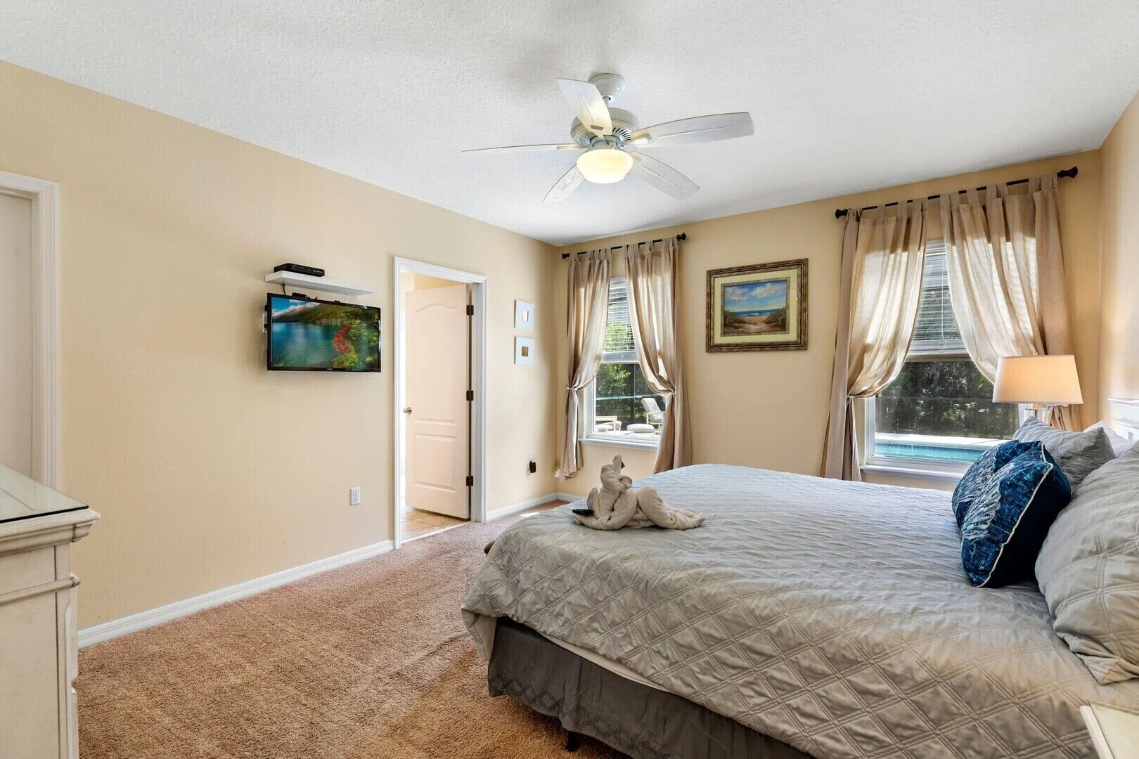 A bedroom with a bed, a ceiling fan, a window with curtains, and a painting on the wall.