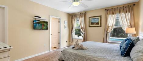 A bedroom with a bed, a ceiling fan, a window with curtains, and a painting on the wall.