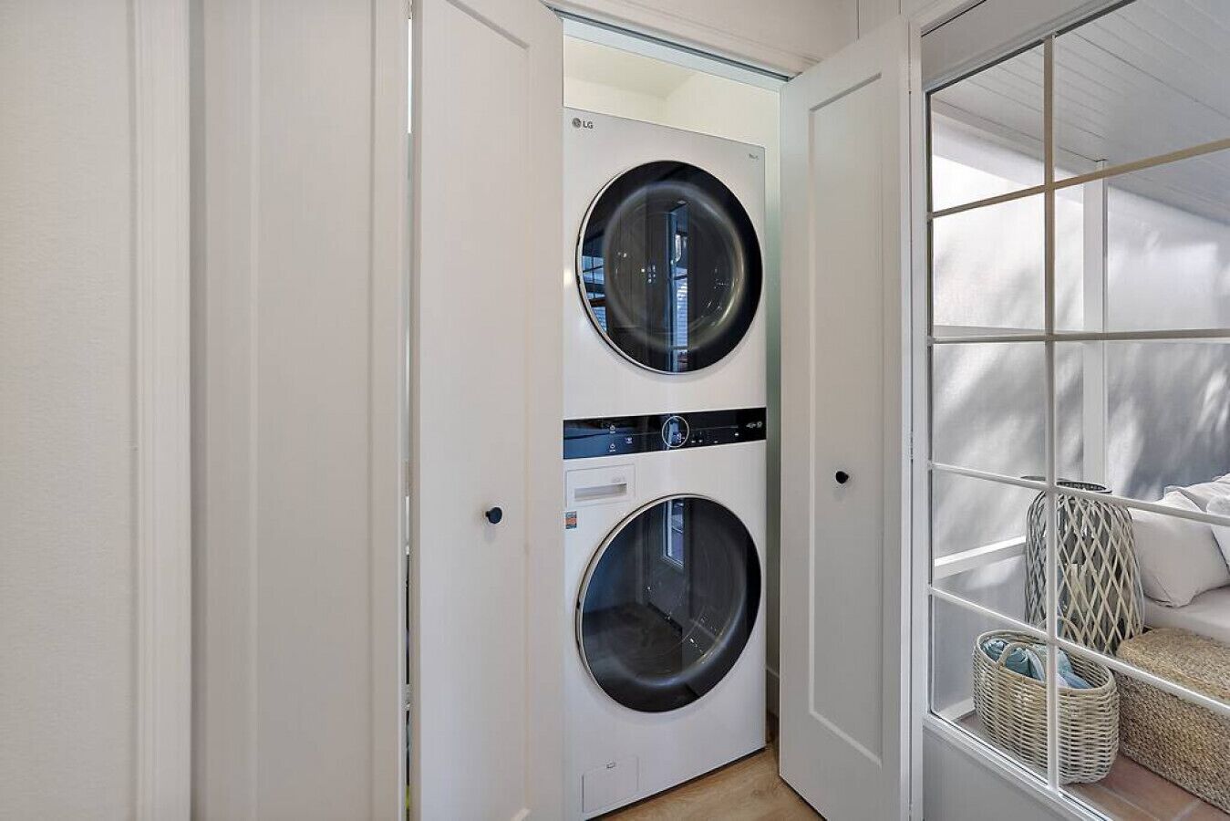 A laundry room with two LG front-loading washing machines, a wicker basket, and a bed with white bedding.