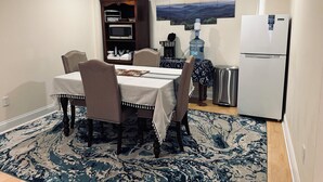 Un comedor con una mesa preparada para cuatro personas, un dispensador de agua, un microondas y un refrigerador.
