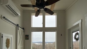 A bedroom with a large bed, a ceiling fan, and a view of a grassy field through a large window. - Luxury Tiny Home with River Views on 300 Acre Ranch (Decatur)