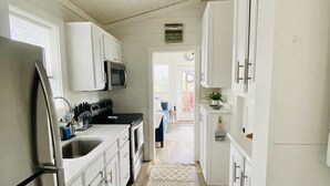 A narrow kitchen with white cabinets, a stainless steel refrigerator, and a microwave. A patterned rug runs down the center of the floor. - Luxury Tiny Home with River Views on 300 Acre Ranch (Decatur)